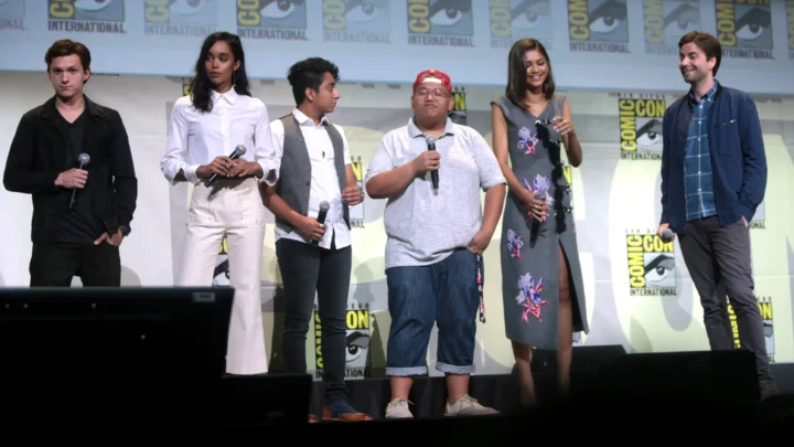 Seis participantes de painel sobre filme de super-heróis posam no palco da Comic-Con International com microfones em mãos