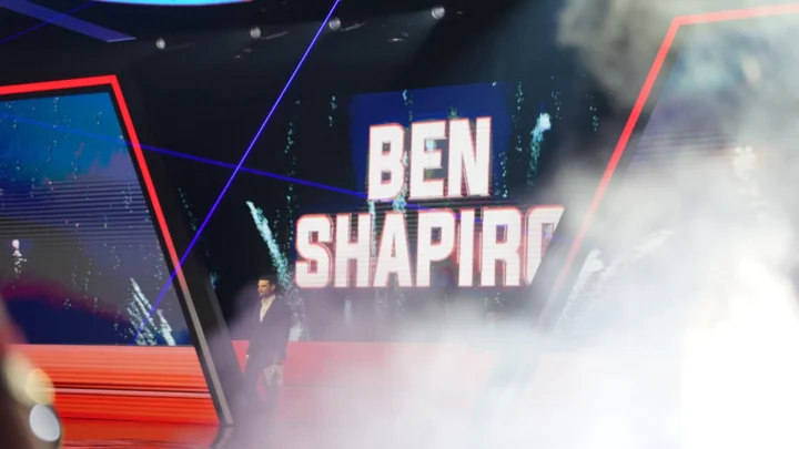 Ben Shapiro em palco do AmericaFest, com o nome do apresentador em letreiro de neon ao fundo