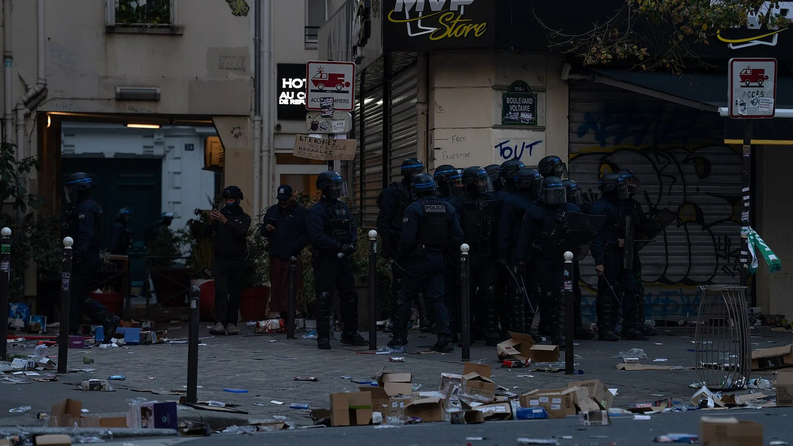 Policiais da tropa de choque diante de uma loja saqueada, com caixas e mercadorias espalhadas pela calçada, em Paris, em 17 de outubro de 2026