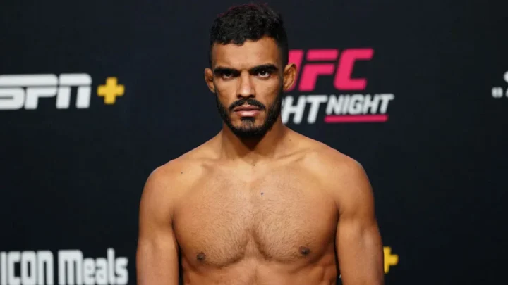 Homem de peito nu, com barba e cabelo escuro, posa em frente a um painel de patrocinadores do UFC Fight Night e da ESPN+ durante a pesagem