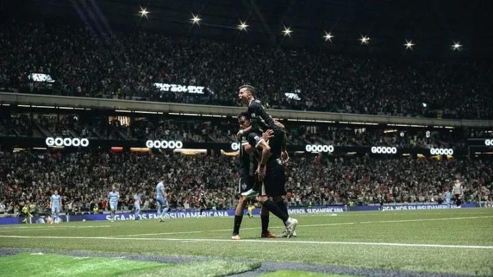 Jogadores do Atlético-MG comemoram um gol em estádio lotado, com o público nas arquibancadas e placas de patrocínio ao redor do gramado