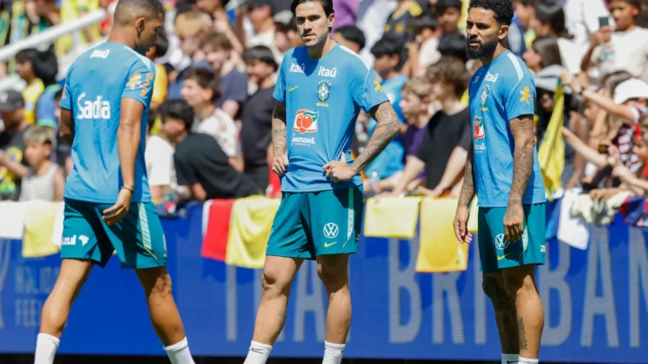 Jogadores da seleção brasileira conversam em campo durante treinamento com torcedores ao fundo nas arquibancadas
