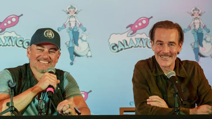 Dois homens seguram microfones durante painel em evento, com cenário ao fundo estampado com personagens de ficção científica e naves espaciais