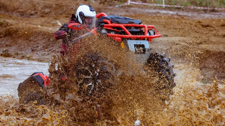 Piloto de capacete branco passa com um quadriciclo vermelho por uma poça e levanta uma parede de lama numa prova de off-road na Rússia, em 2020 (imagem ilustrativa)