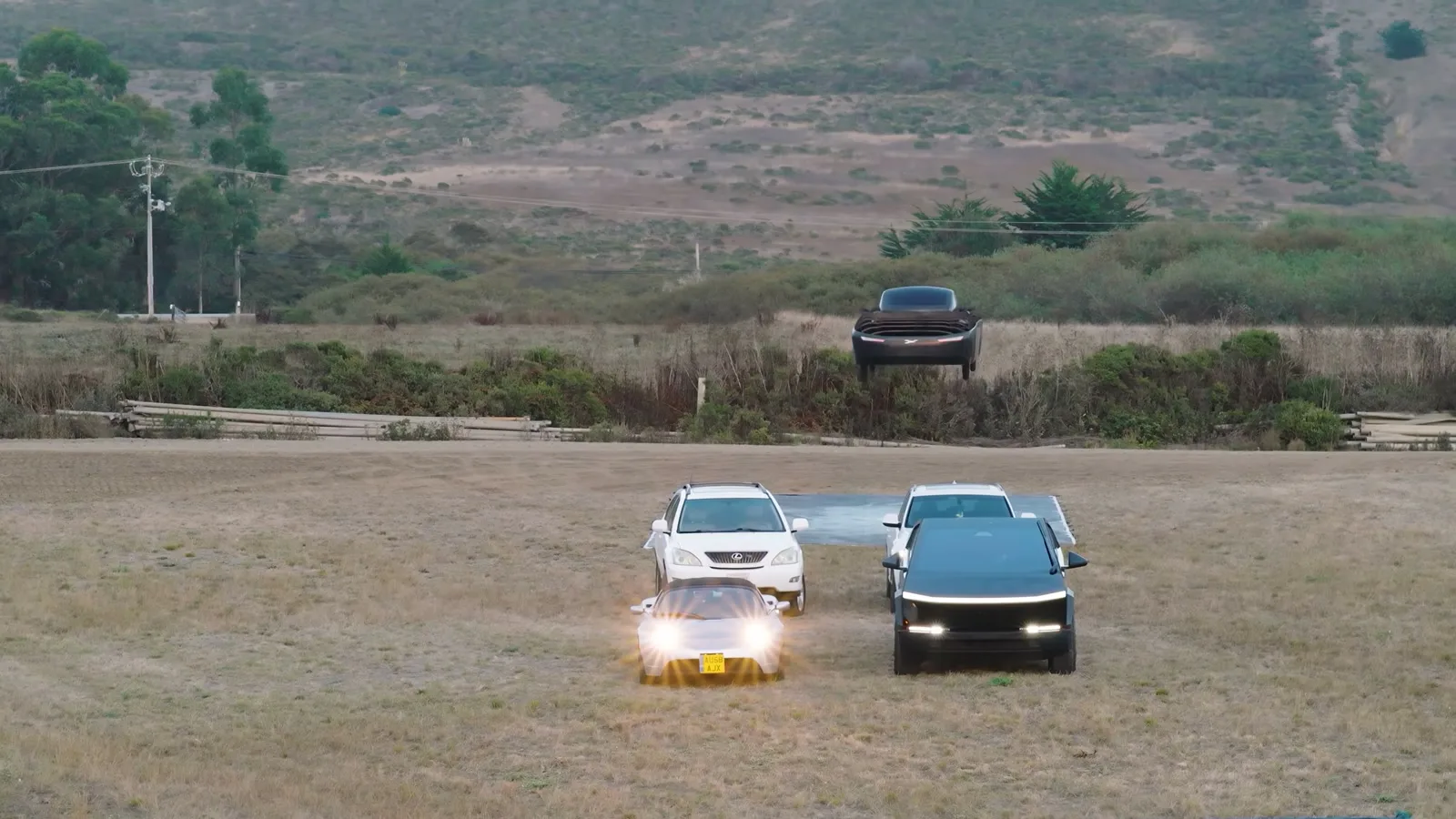 Carro voador da Alef se aproxima voando baixo de um Tesla Roadster, uma Cybertruck e outro carro estacionados no campo