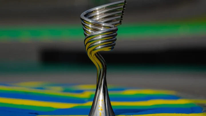 Troféu prateado em espiral, com detalhes dourados na base, posado sobre piso pintado nas cores verde, amarelo e azul