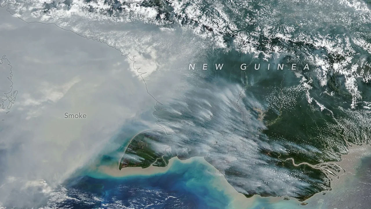 A fumaça cobre grande parte do terço sul da Nova Guiné, enquanto nuvens e cadeias de montanhas que correm no sentido leste-oeste são visíveis na parte norte da ilha.
