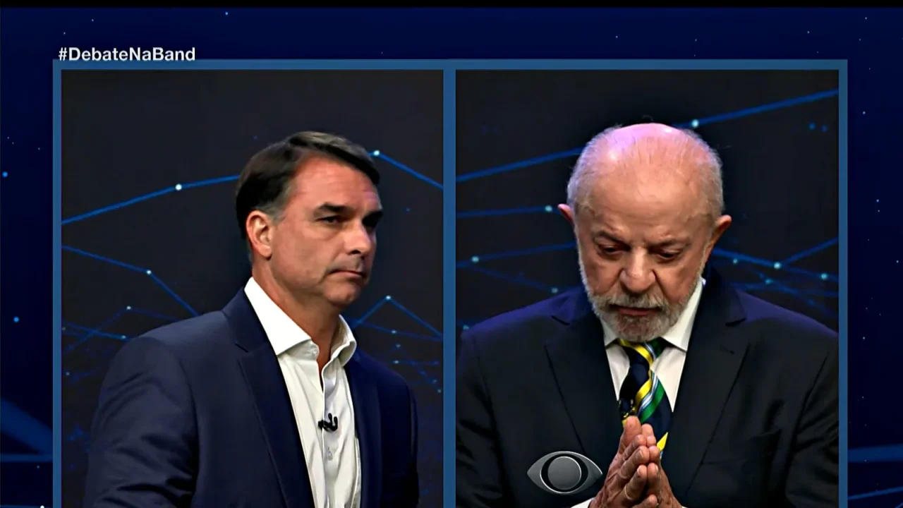 Tela dividida da transmissão: Flávio Bolsonaro à esquerda e Lula à direita, durante a pergunta sobre os Estados Unidos