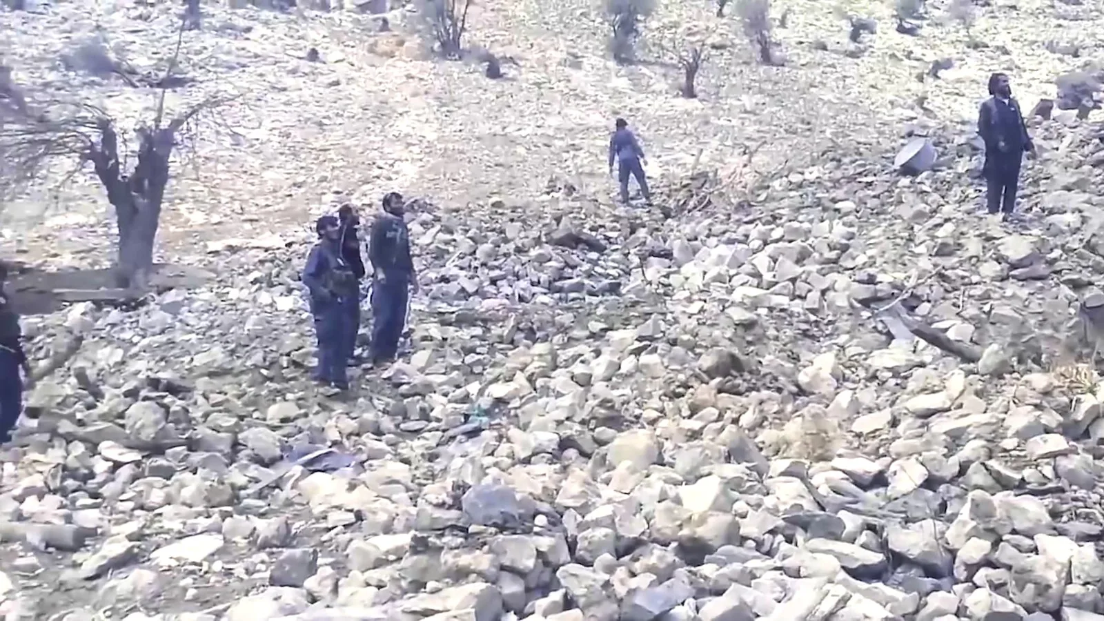 Policiais afegãos caminham sobre pedras e árvores derrubadas na área atingida pela MOAB no distrito de Achin, em abril de 2017