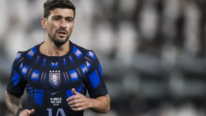 Jogador em uniforme azul e preto com escudo de seleção nacional em partida de futebol