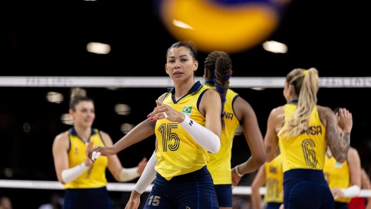 Jogadora de vôlei com uniforme amarelo e azul da seleção brasileira durante partida, com colega ao fundo perto da rede