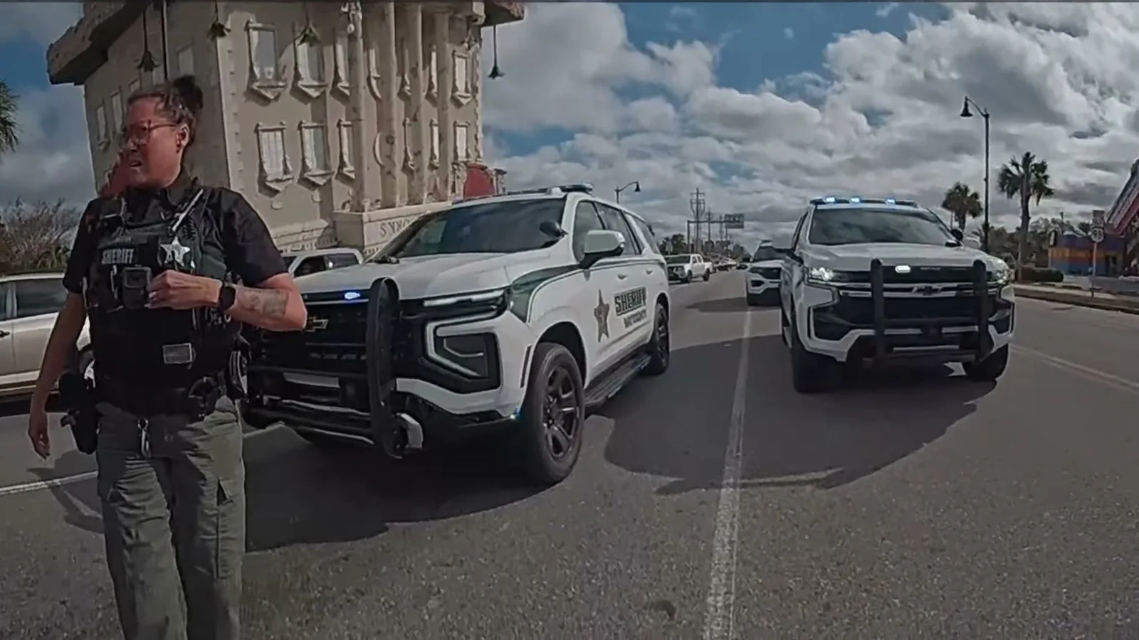 Policial do xerife na avenida, com duas viaturas de luzes acesas atrás, durante a abordagem