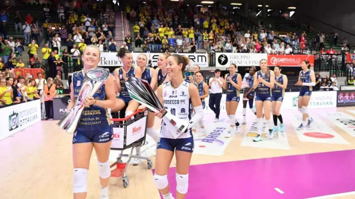 Atletas de voleibol feminino exibem troféus após vitória em partida disputada em ginásio com arquibancadas repletas de torcedores