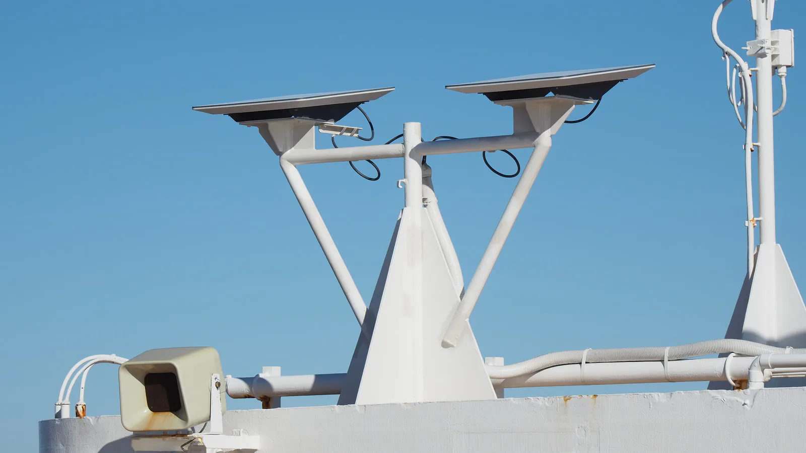 Duas antenas planas da Starlink instaladas num mastro branco de navio, sob céu azul