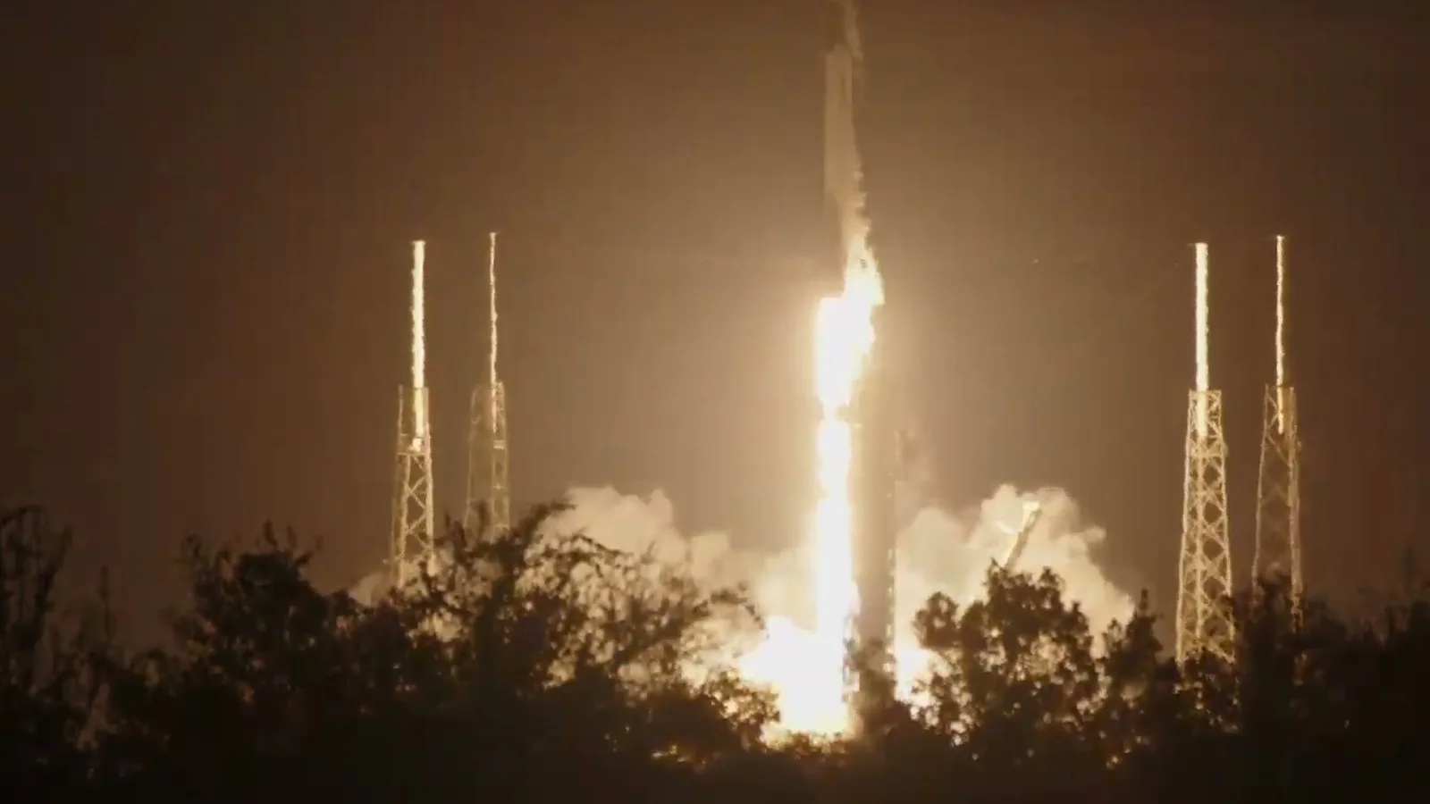 Falcon 9 sobe da plataforma no Cabo Canaveral, iluminando de laranja a fumaça e as torres de para-raios no começo da manhã