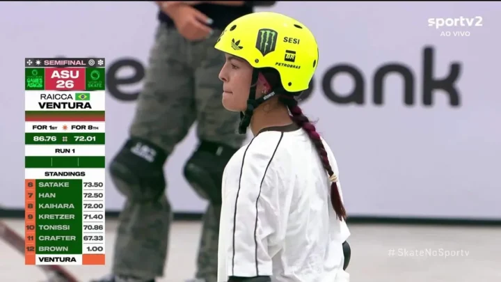Skatista de capacete amarelo e trança observa a pista durante a semifinal do Mundial de Skate Park, com placar de competição exibido ao lado