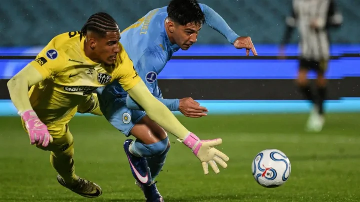 Goleiro do Atlético-MG, de amarelo e luvas rosa, disputa a bola com atacante do City Torque, de azul, em lance dividido no gramado