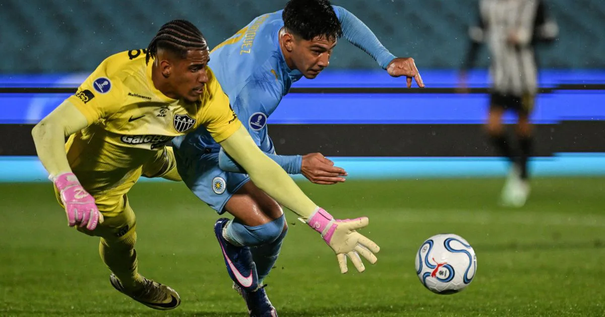 Goleiro do Atlético-MG, de amarelo e luvas rosa, disputa a bola com atacante do City Torque, de azul, em lance dividido no gramado