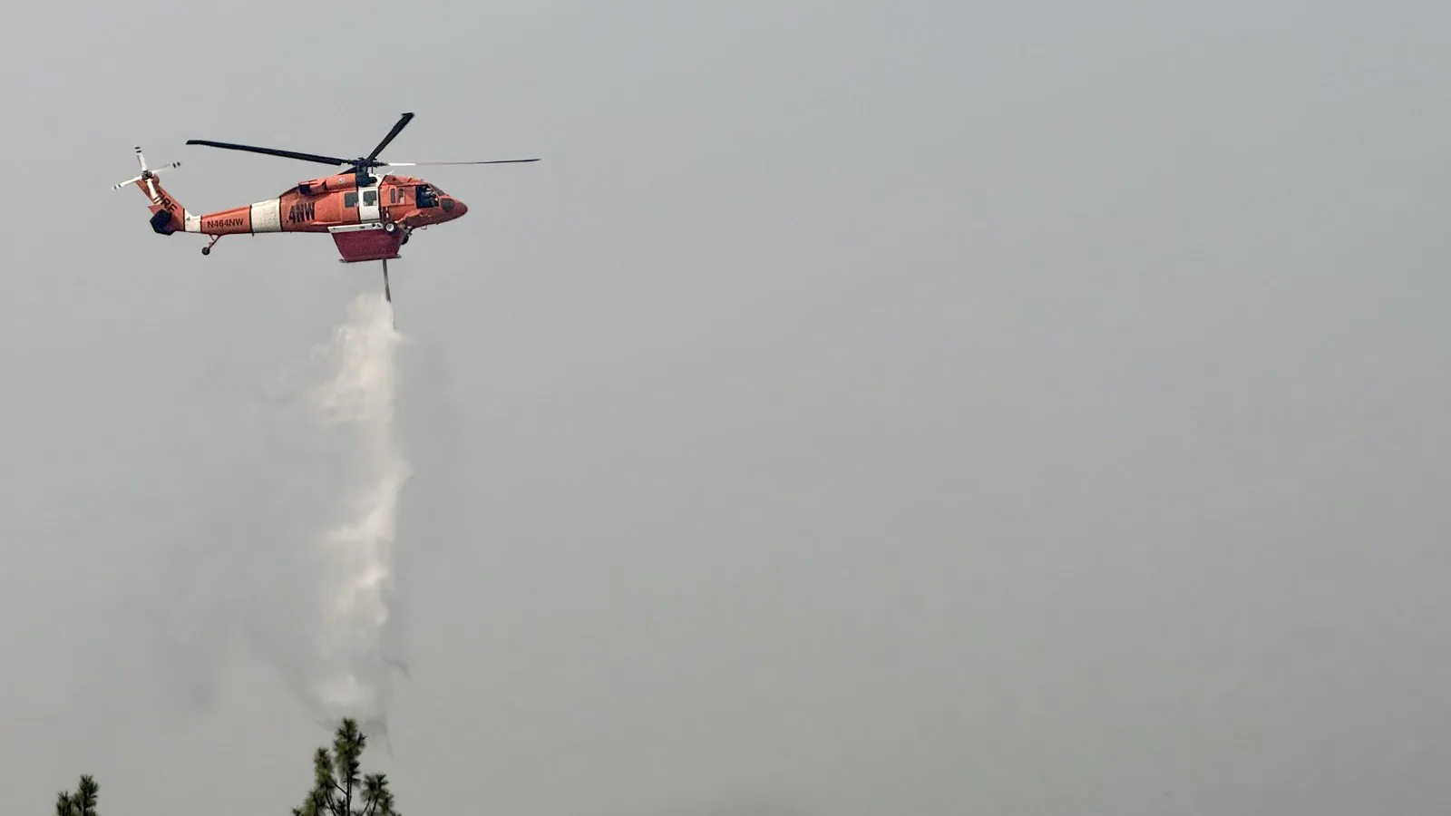 Helicóptero de combate a incêndio solta água sobre o incêndio Autumn Lane, na região de Spokane, em meio à fumaça