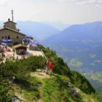 O Kehlsteinhaus, casa de pedra no topo do monte Kehlstein, com guarda-sóis no terraço, visitantes na trilha e os Alpes da Baviera ao fundo, antes do incêndio (imagem de arquivo)