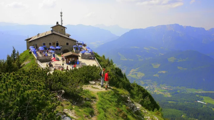 O Kehlsteinhaus, casa de pedra no topo do monte Kehlstein, com guarda-sóis no terraço, visitantes na trilha e os Alpes da Baviera ao fundo, antes do incêndio (imagem de arquivo)