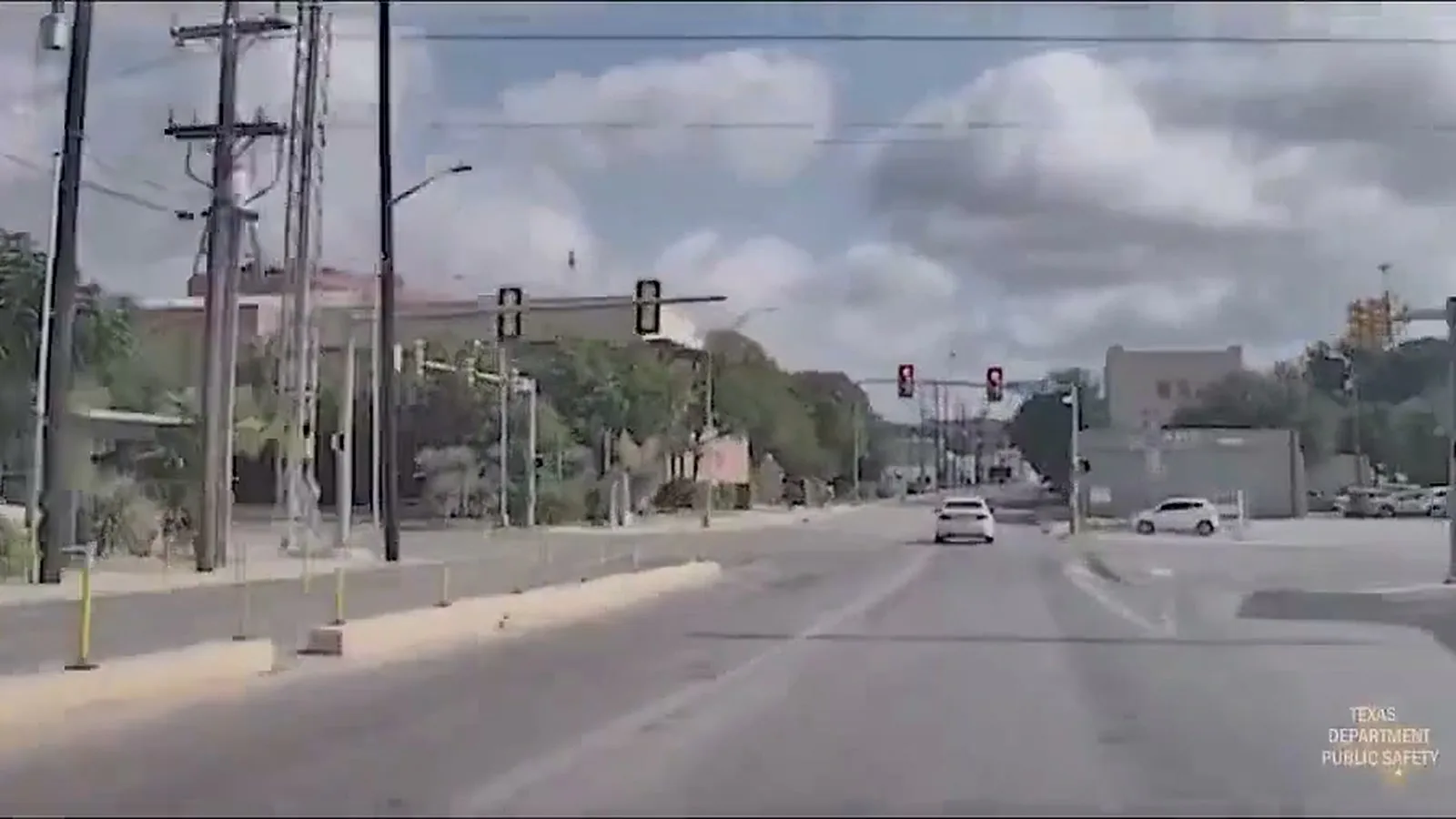 Câmera da viatura do DPS mostra um sedã branco à frente, numa avenida, a caminho de um cruzamento com sinais vermelhos