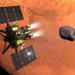 Concepção artística da nave MMX da JAXA durante a inserção na órbita de Marte. A lua marciana Fobos, que a MMX irá explorar e coletar amostras, aparece ao fundo.