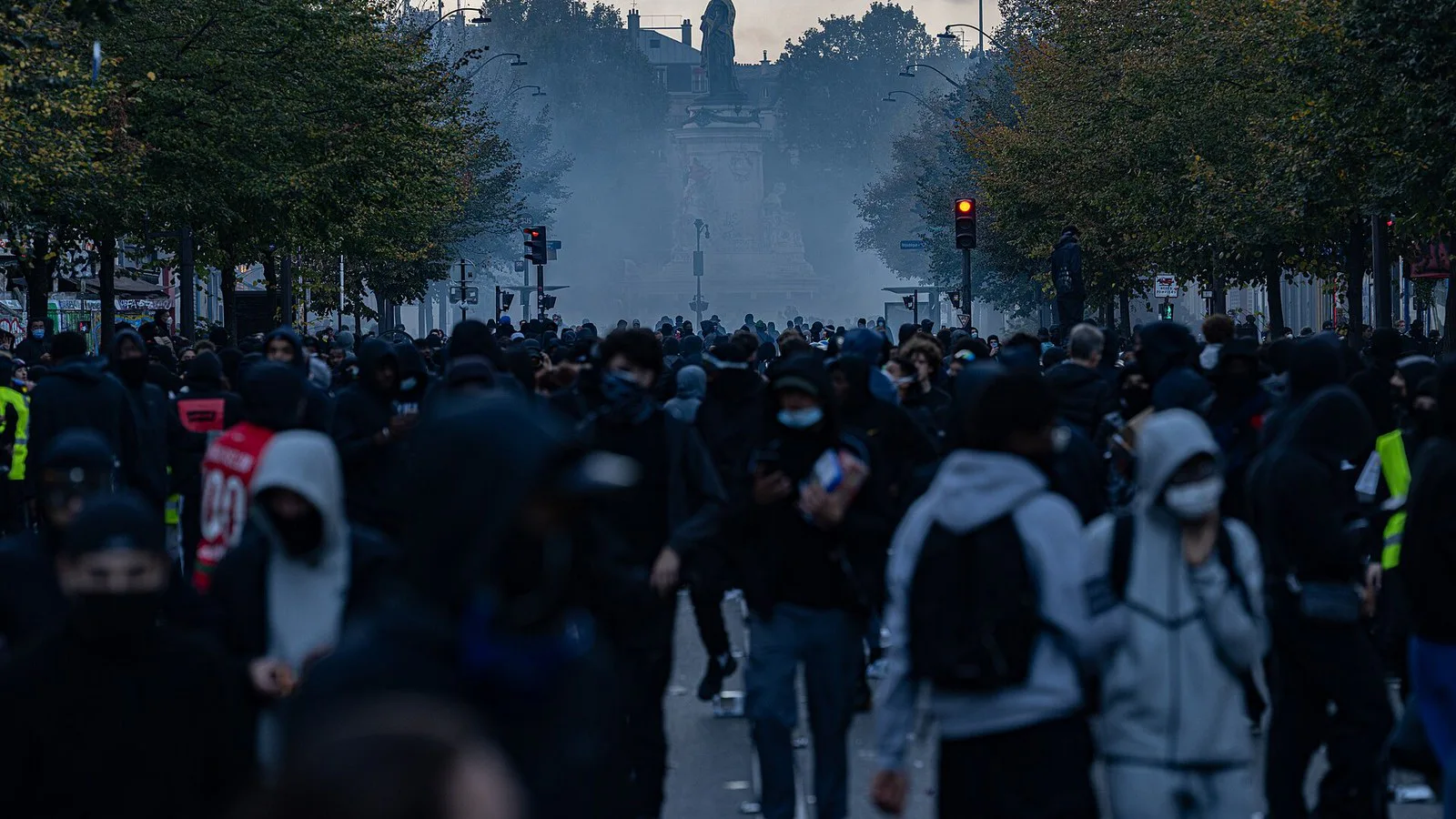 Multidão de encapuzados avança por uma avenida coberta de gás lacrimogêneo perto da Praça da República, em Paris, em 17 de outubro de 2026