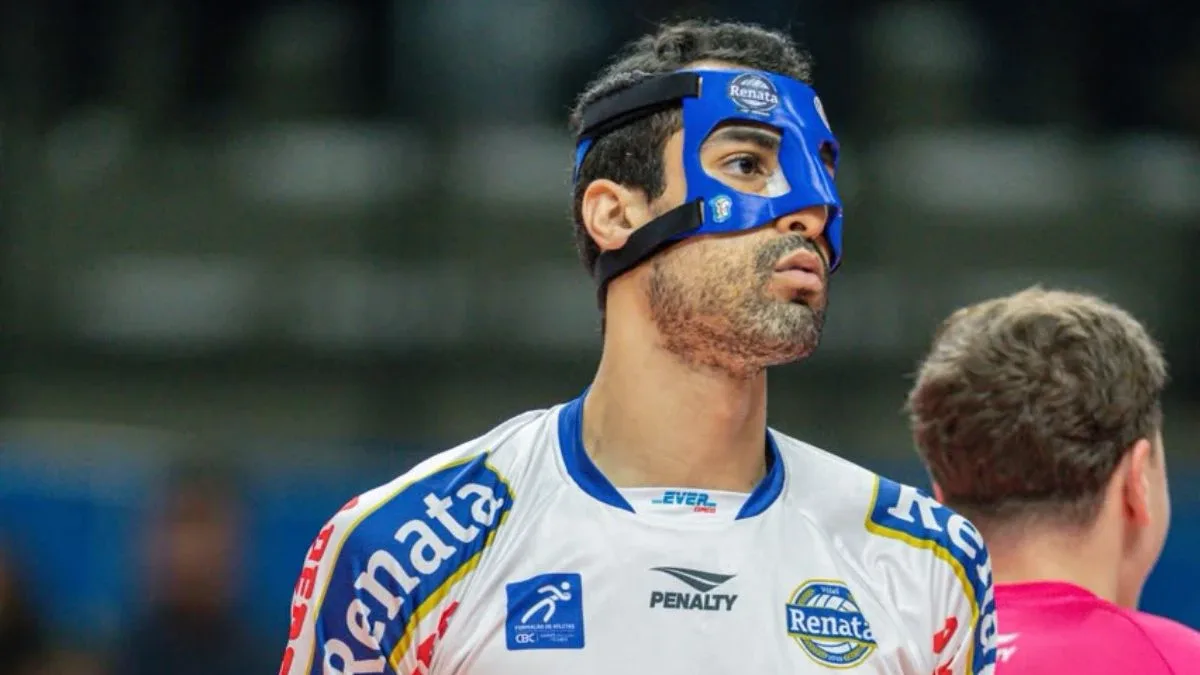 Jogador do Vôlei Renata usa máscara protetora azul no rosto e observa a quadra durante partida, ao lado de um árbitro de camisa rosa