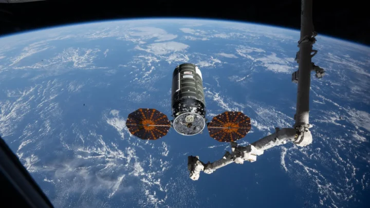 A espaçonave de carga Cygnus XL, da Northrop Grumman, repousa em seu ponto de captura em 13 de abril de 2026, a 12 metros da Estação Espacial Internacional, enquanto o braço robótico Canadarm2 se prepara para capturar a nave de reabastecimento.