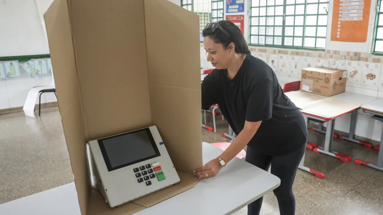 Mesária ajeita a cabine de papelão ao redor de uma urna eletrônica em uma sala de aula de escola pública em Brasília (imagem de arquivo)