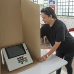 Mesária ajeita a cabine de papelão ao redor de uma urna eletrônica em uma sala de aula de escola pública em Brasília (imagem de arquivo)
