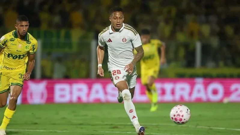 Jogador de camisa branca, número 28, conduz a bola em campo com adversários de amarelo ao fundo, em partida do Brasileirão