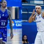 Dois jogadores em quadra durante partida de basquete do NBB, um de uniforme azul-marinho e outro de branco, em ginásio com arquibancadas azuis ao fundo