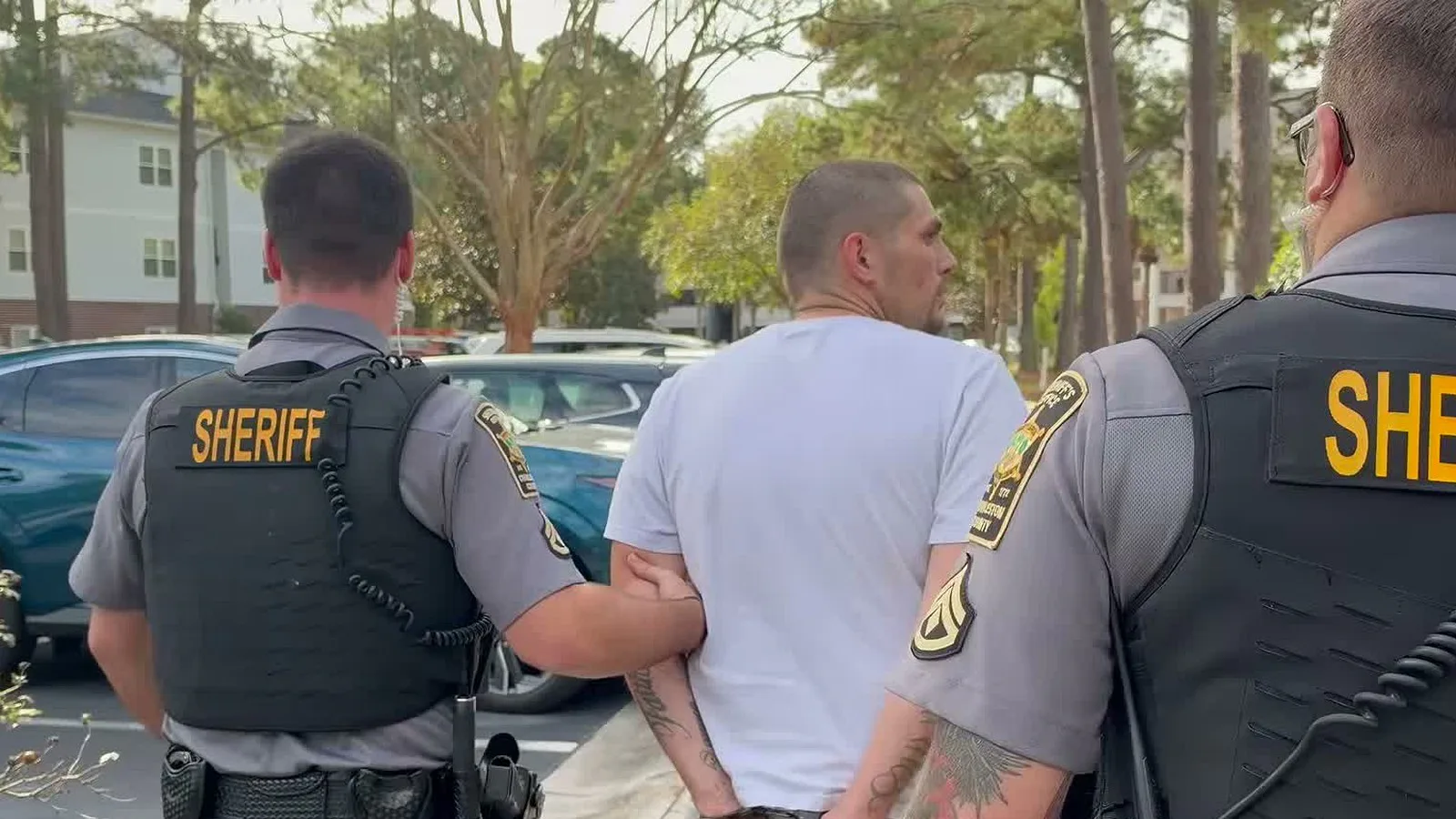 Agentes do xerifado levam pelos braços, algemado, o homem apontado pela polícia como o motociclista