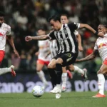 Jogador do Atlético de camisa listrada preta e branca disputa a bola com dois adversários em uniforme branco e vermelho durante partida de futebol em estádio cheio
