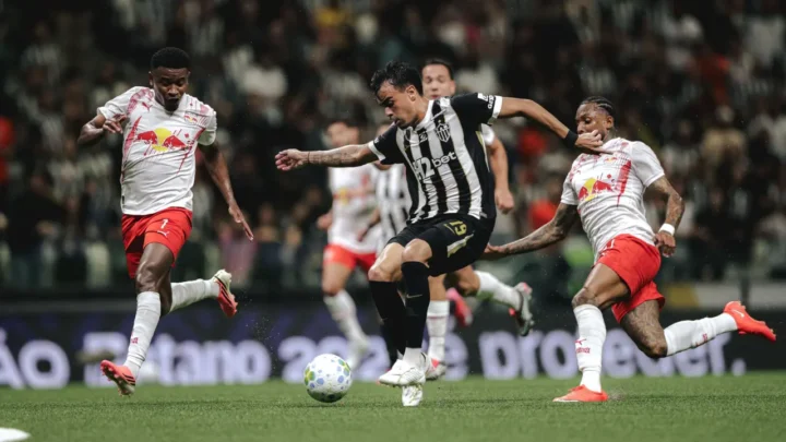 Jogador do Atlético de camisa listrada preta e branca disputa a bola com dois adversários em uniforme branco e vermelho durante partida de futebol em estádio cheio