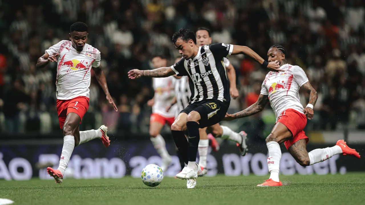 Jogador do Atlético de camisa listrada preta e branca disputa a bola com dois adversários em uniforme branco e vermelho durante partida de futebol em estádio cheio