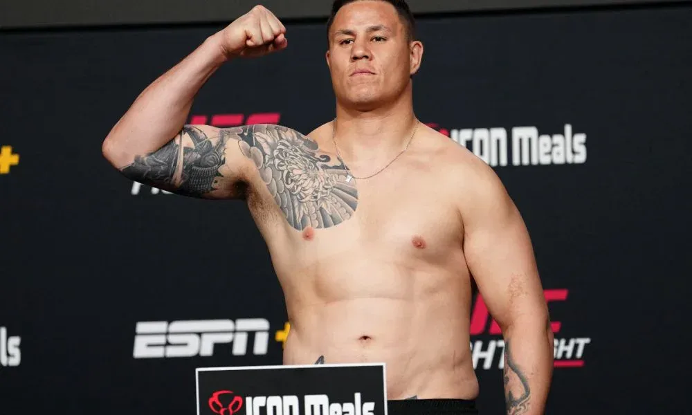 Homem sem camisa, com tatuagens no braço e no peito, flexiona o bíceps diante de painel com logos da ESPN e do UFC durante a pesagem