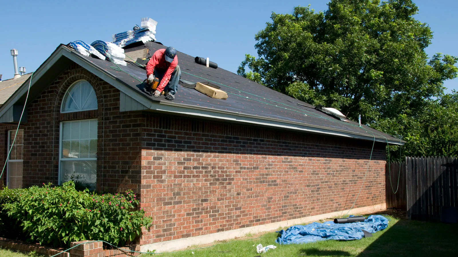 Telhadista de boné, agachado, troca o telhado de uma casa de tijolos em Norman, Oklahoma, danificada por tornados, em 2010 (imagem ilustrativa, sem relação com a operação)