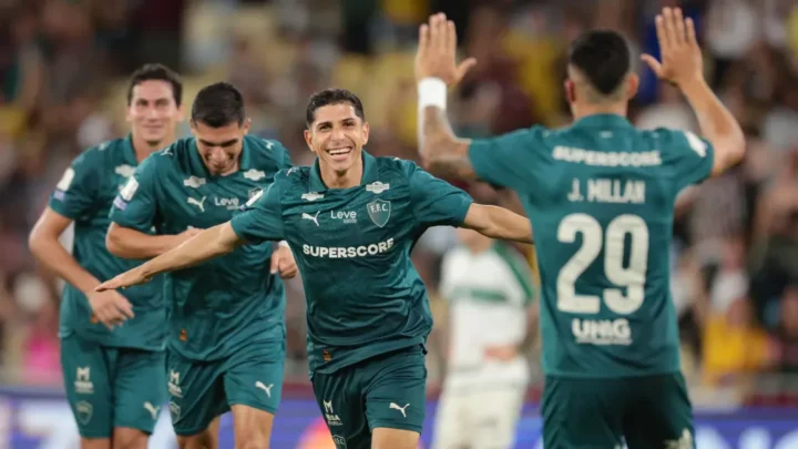 Jogadores de camisa verde comemoram um gol de braços abertos, com um jogador de costas erguendo as mãos e o uniforme trazendo o nome J. Millan, número 29