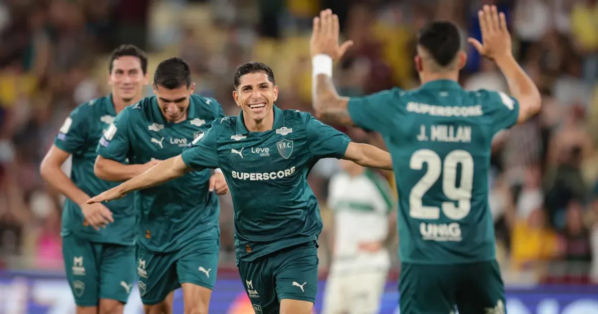Jogadores de camisa verde comemoram um gol de braços abertos, com um jogador de costas erguendo as mãos e o uniforme trazendo o nome J. Millan, número 29