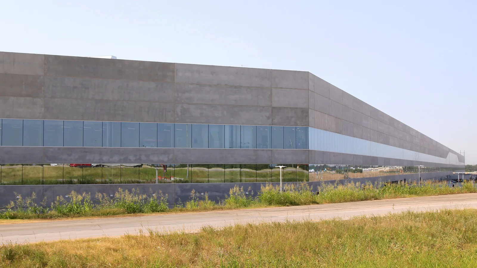 Prédio da Gigafactory da Tesla no Texas, com fachada de concreto e vidro e gramado à frente, em foto de junho de 2022