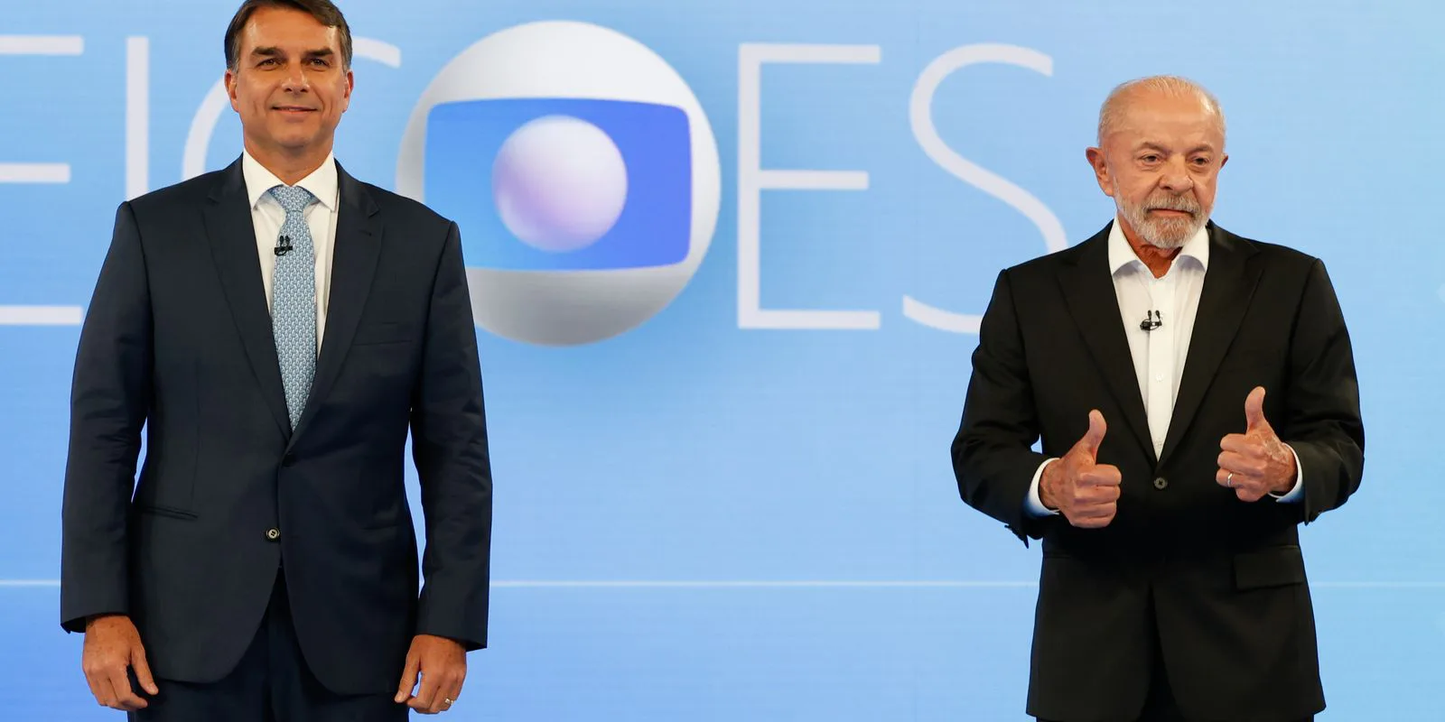 Flávio Bolsonaro, à esquerda, e Lula, que faz sinal de positivo com as duas mãos, posam no cenário do debate da TV Globo, no Rio de Janeiro, em 23 de outubro de 2026