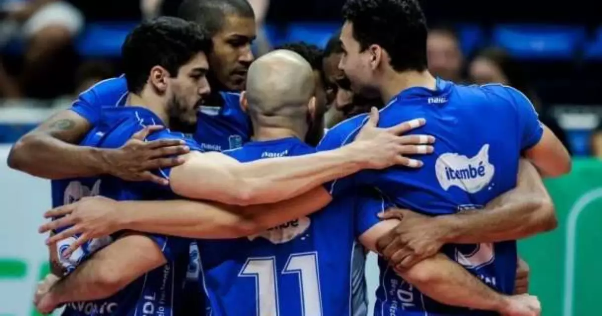Jogadores de vôlei em uniforme azul formam roda no centro da quadra durante partida do Campeonato Mineiro Masculino