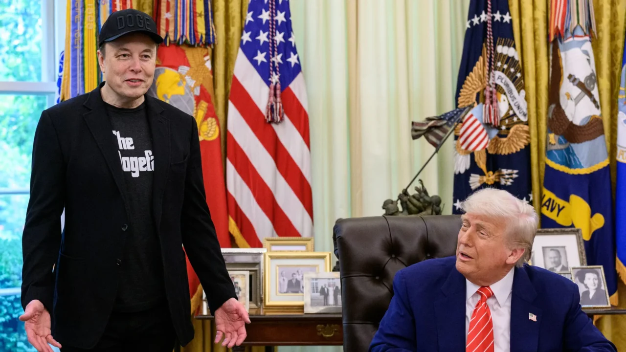 Elon Musk, de boné preto com a palavra DOGE e paletó preto, fala de pé no Salão Oval ao lado de Donald Trump, sentado à mesa, na entrevista de despedida de Musk do governo, em 30 de maio de 2025 (imagem de arquivo)