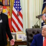 Elon Musk, de boné preto com a palavra DOGE e paletó preto, fala de pé no Salão Oval ao lado de Donald Trump, sentado à mesa, na entrevista de despedida de Musk do governo, em 30 de maio de 2025 (imagem de arquivo)