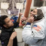 A astronauta da NASA Jessica Watkins auxilia o astronauta da NASA Luke Delaney enquanto ele pratica como vestir um traje espacial em um simulador de câmara de descompressão da Estação Espacial Internacional em 5 de maio de 2026, na Instalação de Maquetes de Veículos Espaciais do Centro Espacial