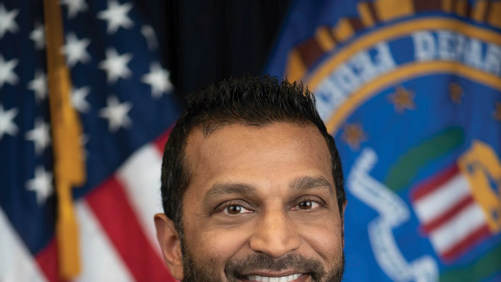 Retrato oficial do diretor do FBI, Kash Patel, de terno escuro, diante da bandeira americana e do selo do FBI