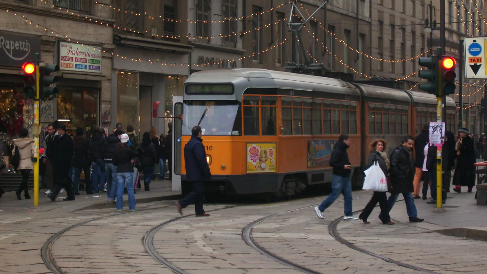 Bonde laranja e pedestres na esquina da Piazza del Duomo com a Via Torino, no centro de Milão, em 2006 (imagem de arquivo)